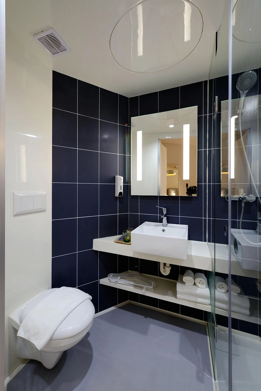 Modern Chicago bathroom with dark tile walls, illuminated mirror, white vanity, and a glass shower enclosure.