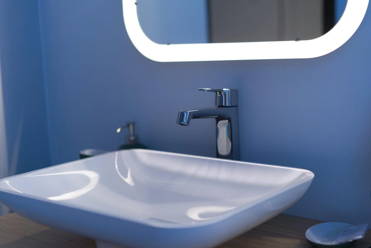 “Close-up of a modern bathroom sink with chrome faucet and soft mirror lighting against a blue accent wall.