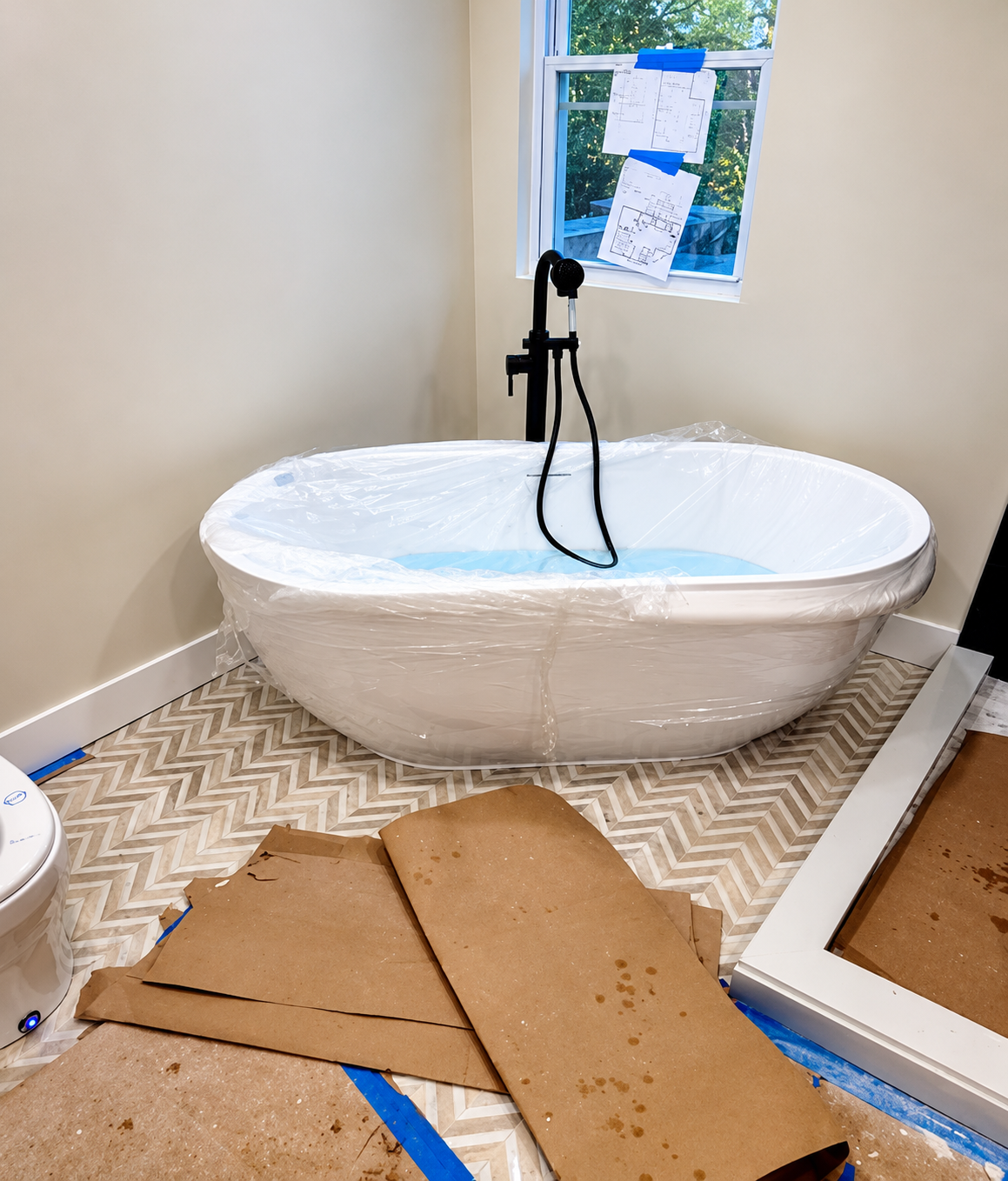 Bathroom remodeling work in progress by Silvestre Construction, showing a freestanding bathtub, black faucet, herringbone tile flooring, and protective construction materials.