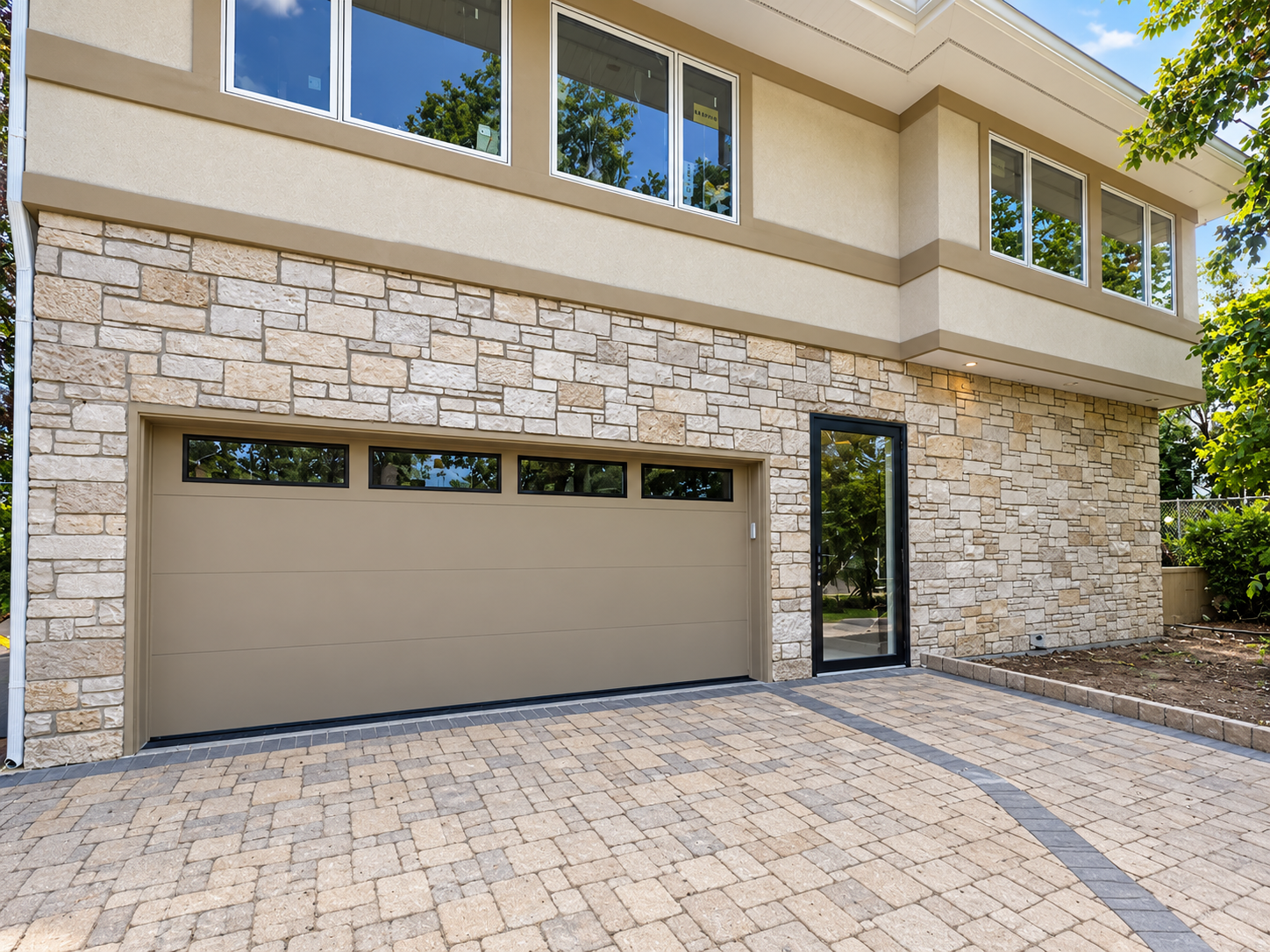 Two-story home exterior with stone facade, garage door, and paved driveway showcasing residential remodeling work by Silvestre Construction